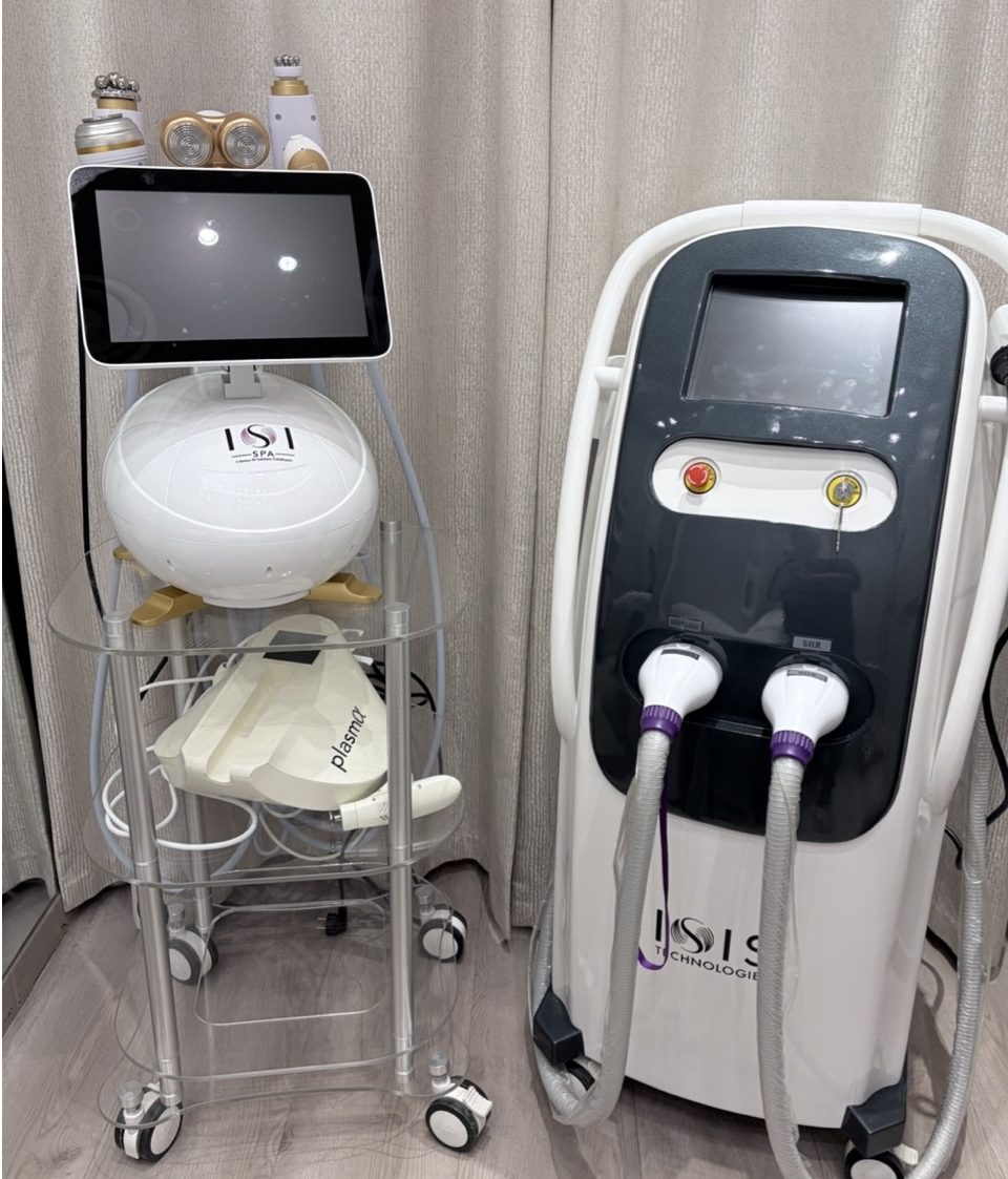 Deux appareils de technologie esthétique, l'un avec un écran tactile et des accessoires au-dessus, l'autre avec des tuyaux et des boutons, situés à côté d'un mur à rideaux.